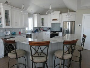 A modern kitchen with white cabinets, a central island with bar stools, stainless steel appliances, and pendant lighting. - 5 bedroom accommodation in Surf City (Surf City)