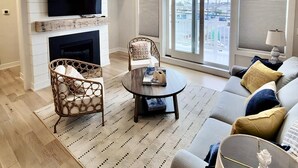 A living room with a fireplace, a ceiling fan, a television, a sofa, and a large window with a view. - Ocean view vacation rental on LBI (Ship Bottom)