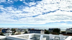 A rooftop terrace with white chairs, a view of the ocean, and houses in the background. - Ocean view vacation rental on LBI (Ship Bottom)