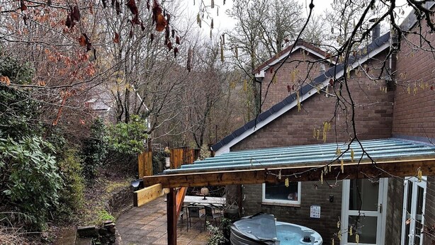 Een achtertuin met een jacuzzi, terrasmeubilair en een houten pergola.