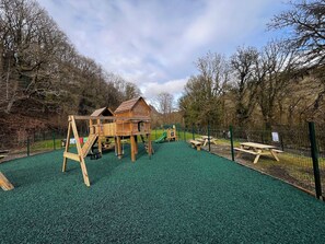 Ein Spielplatz mit einer Holz-Kletterkonstruktion, einer Rutsche und Picknicktischen.