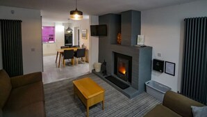 Een moderne woonkamer met een open haard, een eethoek en een keuken op de achtergrond.