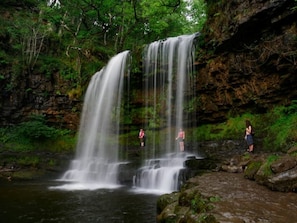 A waterfall in a forested area with rocky terrain and a small stream at the base.