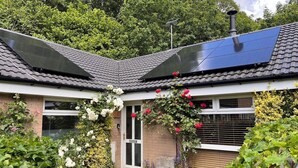 Een huis met een dakbedekt met zonnepanelen, een voordeur en een tuin vol planten en bloemen.