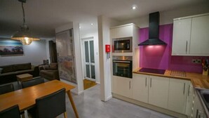 Een moderne keuken met een magnetron, oven en een zwarte afzuigkap. Er is een eethoek met een houten tafel en stoelen.