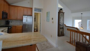 A kitchen with wooden cabinets, a stainless steel refrigerator, a granite countertop, a wooden stool, and a view of the living area. - Ocean Front Single Family Home located in Beach Haven Gardens (Beach Haven Gardens)