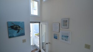 A hallway with a door leading to a balcony, a painting of a turtle, and several framed pictures on the wall. - Ocean Front Single Family Home located in Beach Haven Gardens (Beach Haven Gardens)