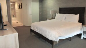 Un dormitorio con cama, mesita de noche, lámpara, ventilador de techo, puerta a un baño y un pequeño escritorio con silla.