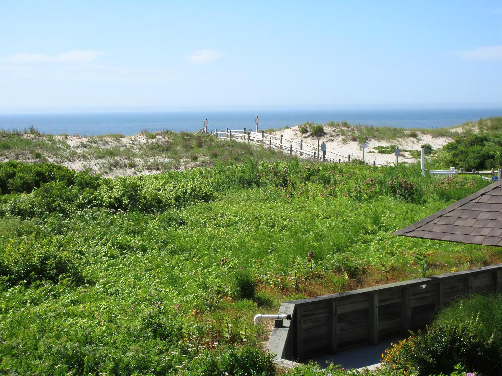 A coastal landscape with a wooden fence, sandy dunes, and a view of the sea.