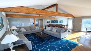 A spacious living room with a high ceiling and exposed wooden beams, a gray sectional sofa, a coffee table, and a blue patterned rug. - 5 BRs, Hot Tub Roof Top, 2nd off the Ocean. (Loveladies)