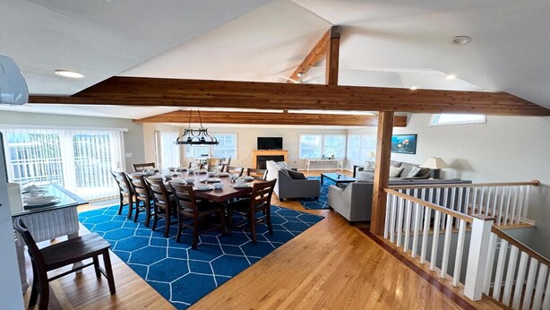 A spacious dining area with a high ceiling and exposed wooden beams, a living room with a fireplace, and a staircase with a railing. - 5 BRs, Hot Tub Roof Top, 2nd off the Ocean. (Loveladies)