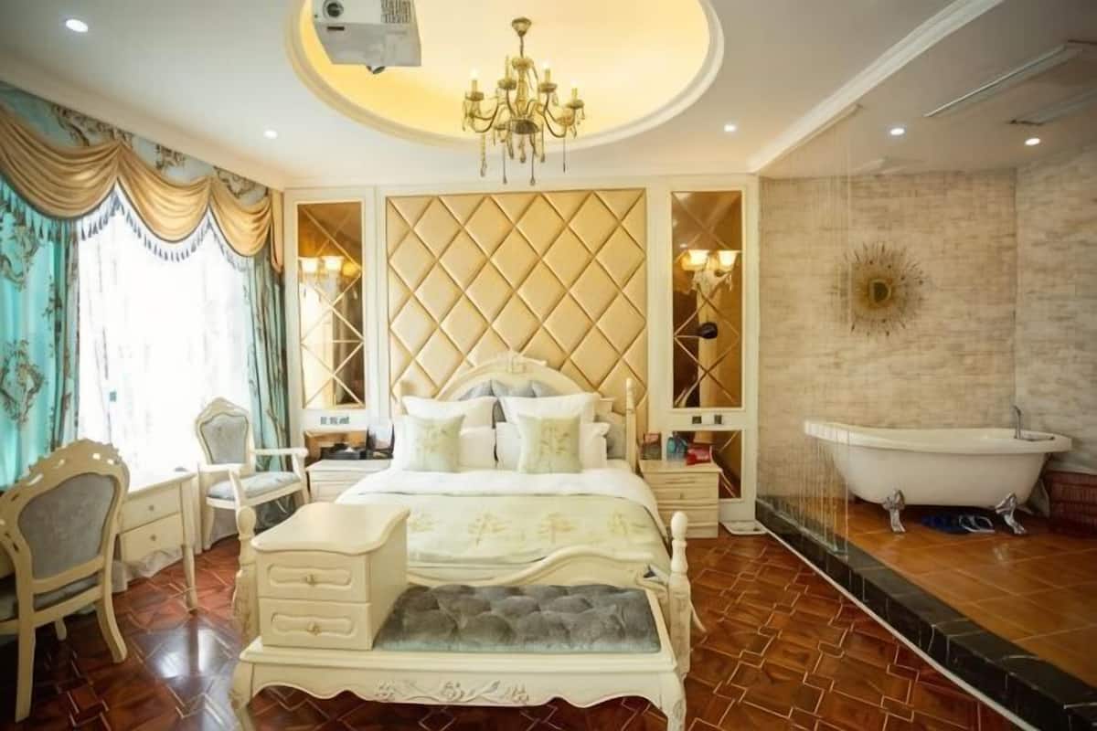 A bedroom with a large bed, a chandelier, a bathtub, and a decorative wall panel.