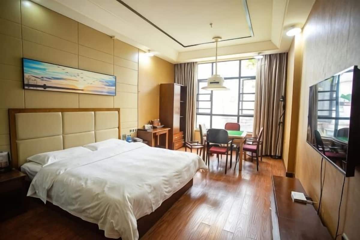 A hotel room with a bed, a desk, a chair, a TV, and a painting on the wall.
