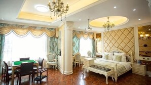 A spacious bedroom with a large bed, a desk, and a chair, a chandelier, and a decorative ceiling. - Impression Theme Hotel (Nan County)