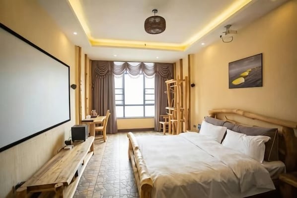 A hotel room with a bed, a desk, a chair, a projector screen, and a large window with curtains.