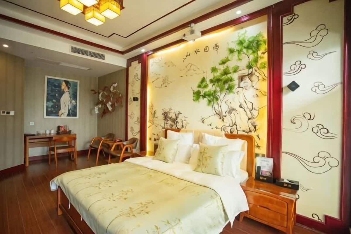 A bedroom with a large bed, a desk, chairs, and a wall with a mural.