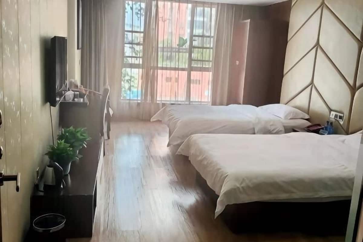 A hotel room with two beds, a wooden floor, a TV on the wall, and a window with curtains.