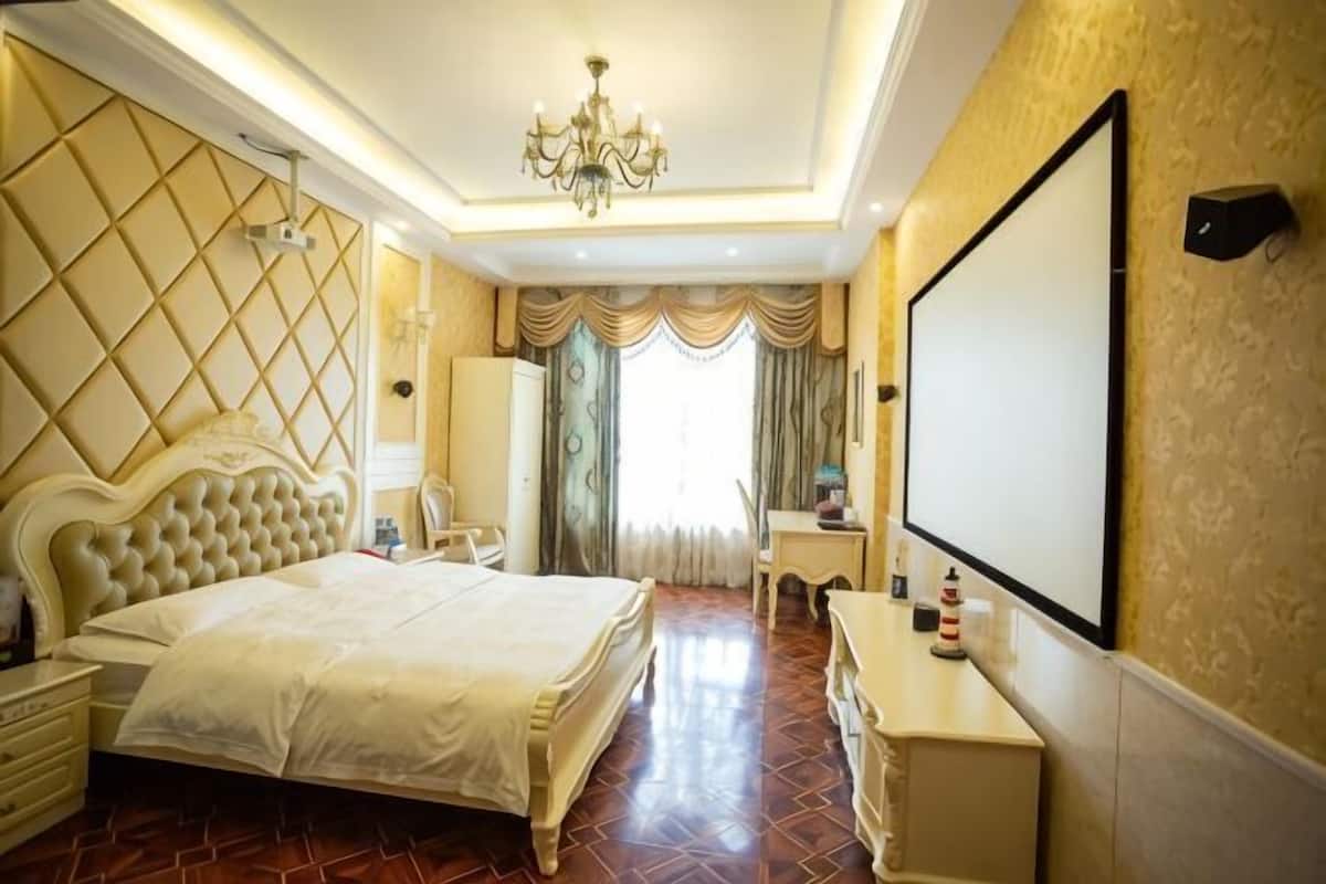 A hotel room with a large bed, a desk, a chair, a TV, and a chandelier.