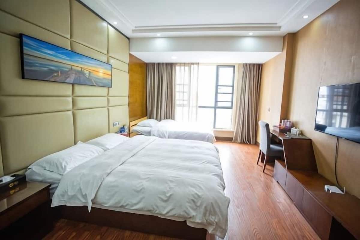 A hotel room with two beds, a desk, a TV, and a painting on the wall.