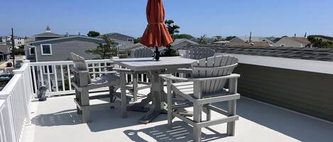 Una terraza en la azotea con una mesa, sillas y una sombrilla, con vistas a casas cercanas.