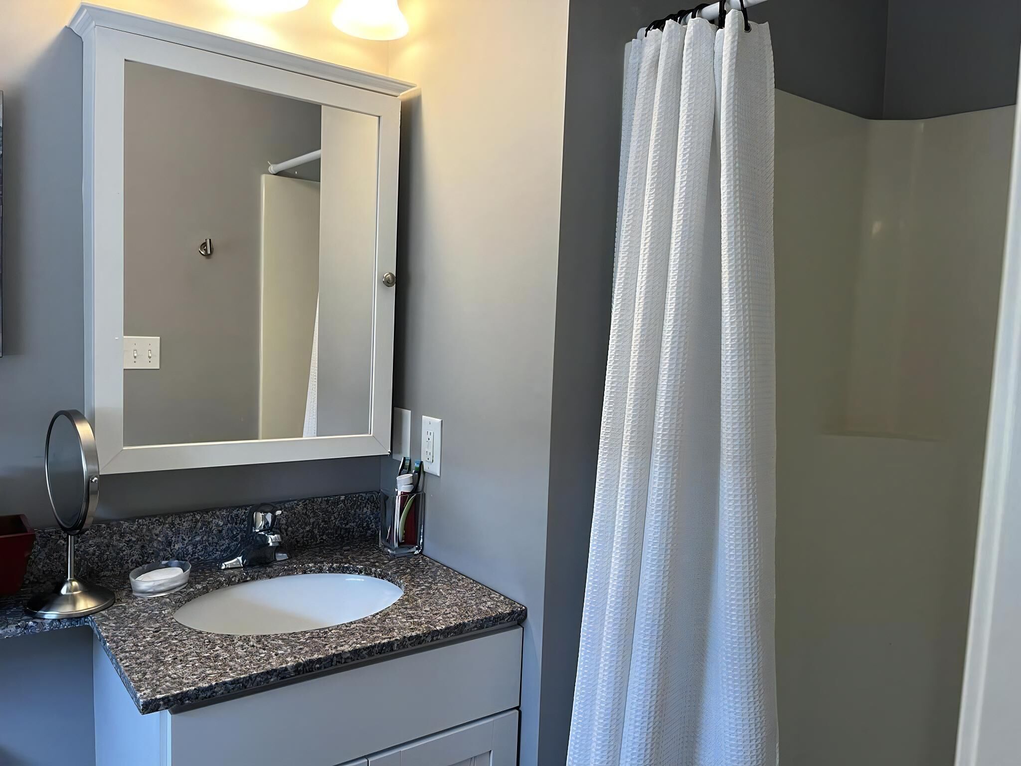A bathroom with a granite countertop sink, a mirror, and a shower curtain.