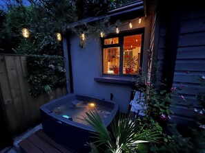 A hot tub outside a house with a window, surrounded by plants and string lights. - Beili Glas Cottage - Hideaway near nature. (Ynysmeudwy)