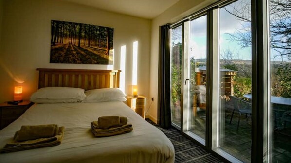 A bedroom with a large bed, two bedside lamps, a painting on the wall, and a view through a sliding glass door to an outdoor area.