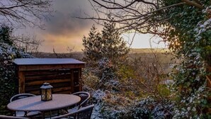 Eine Holzhütte mit Tisch und Stühlen, umgeben von schneebedeckter Vegetation und Blick auf die Landschaft.