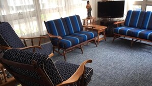 Een woonkamer met een bank, fauteuils, een televisie en een lamp.