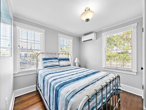 Ein Schlafzimmer mit Bett, Fenster mit Jalousien, Klimaanlage und Deckenleuchte.