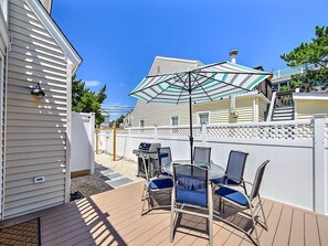 Eine Terrasse im Freien mit Tisch, Stühlen, einem Grill und einem weißen Zaun.