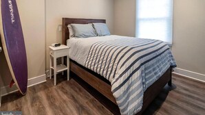 Een slaapkamer met een bed, een nachtkastje, een surfplank en een raam.