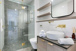 A modern bathroom with a glass-enclosed shower, a white toilet, a vanity with a round sink, and a mirror above the sink. - Oceanfront 3-Bed with Stunning Views, Pool & Sauna (Surfers Paradise)