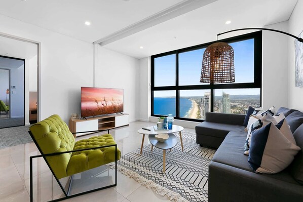 A modern living room with a large window, a television, a sofa, and a green chair. - Oceanfront 3-Bed with Stunning Views, Pool & Sauna (Surfers Paradise)