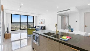 Une cuisine moderne dotée d’un grand îlot central, d’un four encastré et offrant une vue sur la ville grâce à de grandes fenêtres.