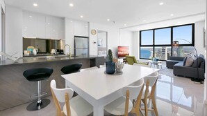 Une cuisine moderne avec des meubles blancs, un îlot central et un coin repas comprenant une table et des chaises blanches.