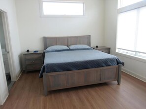 A bedroom with a wooden bed, a nightstand, a dresser, and a window with blinds.