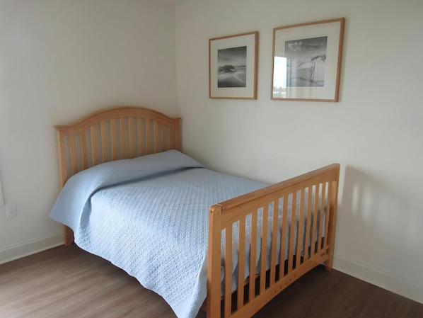 Un lit simple avec une tête de lit et un pied de lit en bois, une couvre-lit bleu clair et deux tableaux encadrés accrochés au mur.