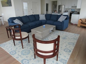 A living room with a blue sectional sofa, two wooden chairs, a coffee table, and a patterned rug.