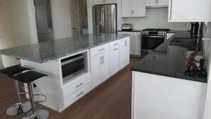 Eine moderne Küche mit weißen Schränken, einer Granit-Arbeitsplatte, Edelstahlgeräten und einem eingebauten Backofen.