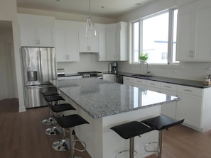 A modern kitchen with white cabinets, a stainless steel refrigerator, a granite countertop, and a large window.