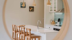 Moderni keittiö, jossa on valkoiset kaapit, keskellä oleva keittiösaareke ja puiset tuolit.