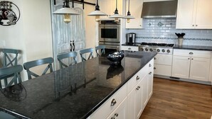 A modern kitchen with a black granite countertop, white cabinets, stainless steel appliances, and pendant lighting.