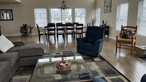 A spacious living room with a high ceiling, a dining area, and large windows.