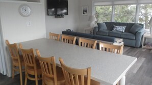 Ett modernt kök med ett matbord och stolar, en platt-TV och ett stort fönster med utsikt över grönområden.
