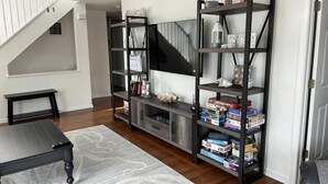 Un salon avec un escalier, une table basse noire, une bibliothèque et une porte.