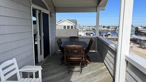 Un espace extérieur abrité, avec une table et des chaises en bois, un banc blanc, et une vue sur la plage et les bâtiments en arrière-plan.