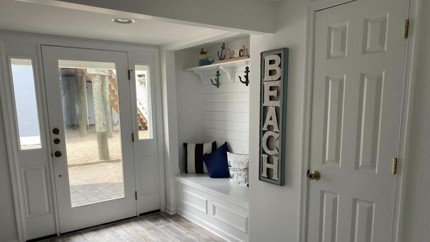 Un couloir doté d’un plancher en bois, de murs blancs et d’un banc agrémenté de coussins décoratifs.