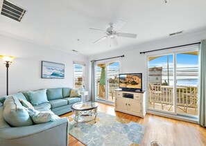 A living room with a sofa, a glass coffee table, a TV, and a balcony with outdoor furniture.
