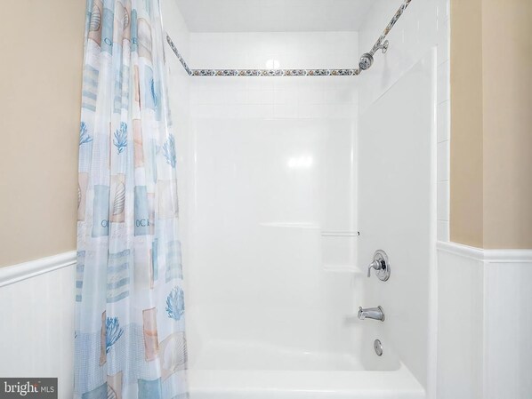 A bathroom with a shower, a curtain with a pattern, and a tiled wall.